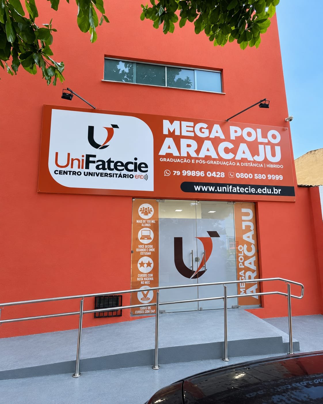 Fachada da unidade de Aracaju: prédio laranja com placa da UniFatecie "Mega Polo Aracaju", porta de vidro e rampa de acesso com corrimão